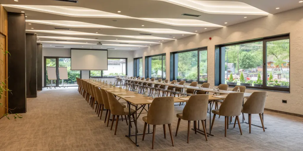 Moderner Konferenzraum mit Reihen von Stühlen und Tischen, großen Fenstern und Projektionstechnik. Optimal für Meetings.