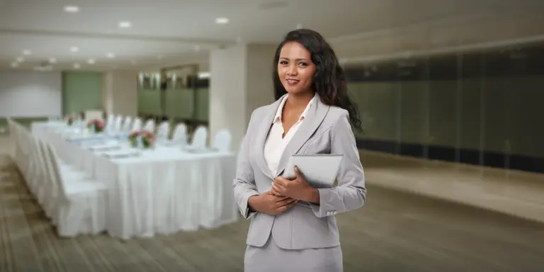 Geschäftsfrau im Anzug mit Tablet, lächelnd vor elegant gedecktem Konferenztisch in modernem, stilvollem Raum.